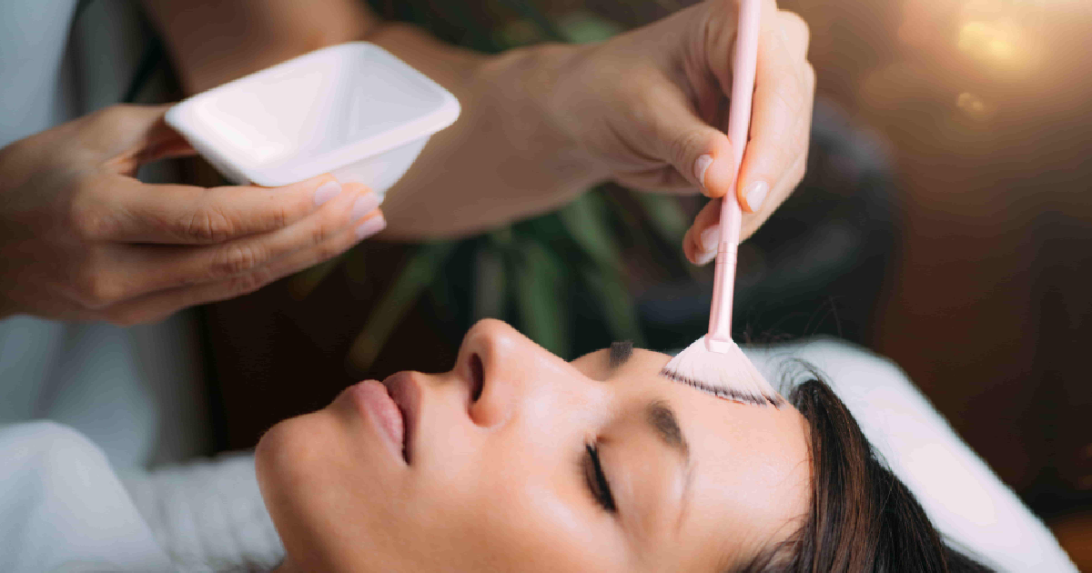 A woman lies with eyes closed while a professional applies a Chemical Peel in Provo, UT using a pink brush.