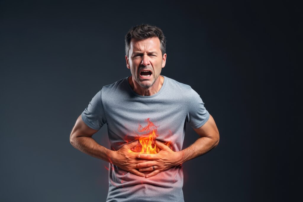 A man clutches his stomach in pain with glowing red flames, symbolizing a digestive health problem.